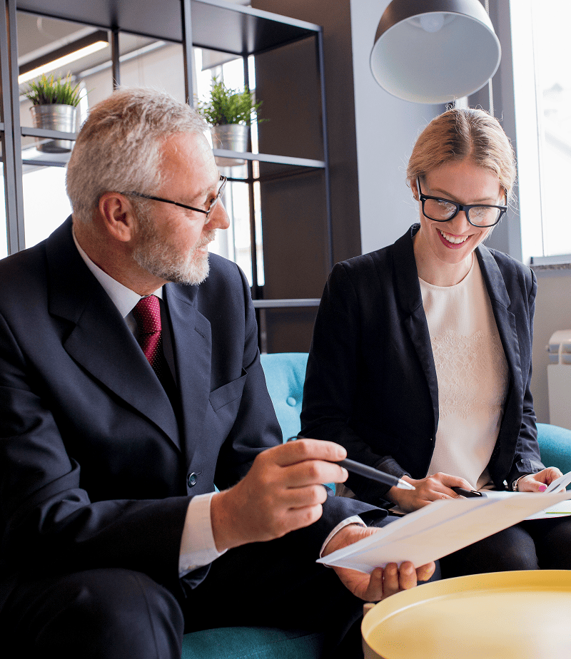 Senior male attorney and younger female client smiling while reviewing adult guardianship legal documents in the office